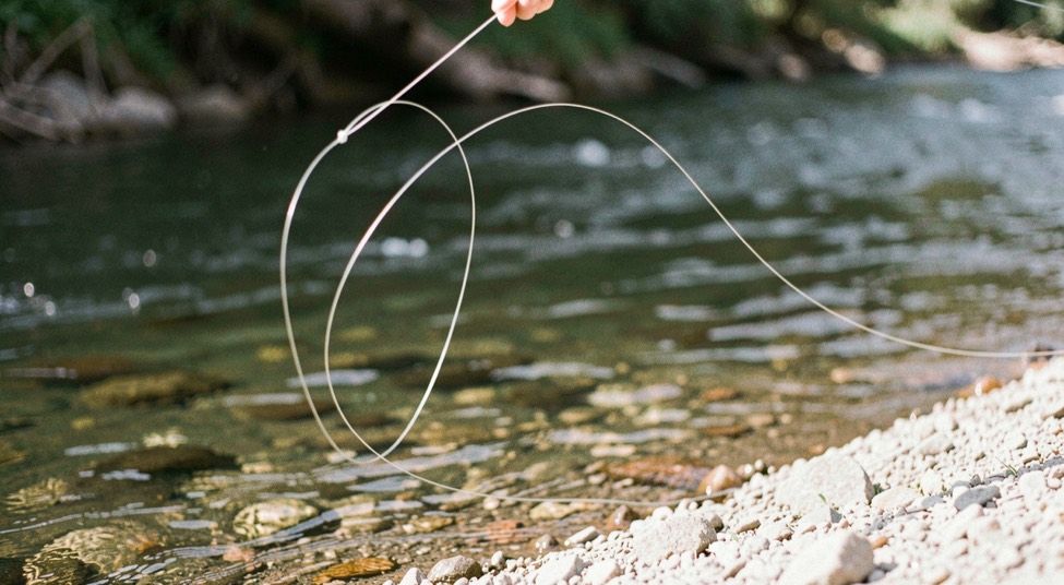 A fly line drawing a clean loop above a shaded run and pale gravel edge, prepared for the fly fishing knots field note